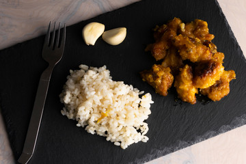 Chicken with orange sauce, rice and garlic on a slate board