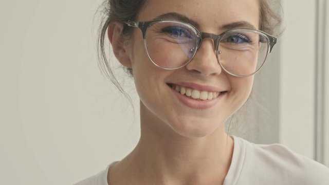 Close up view of happy pretty brunette woman in eyeglasses looking at the camera and winking with eye at home