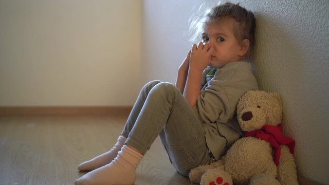  Sad child leaning to the wall by the window. Orphan girl is lonely. Child abuse concept.  Abandoned child.
