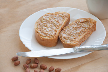 Bread slice with peanut butter, peanuts, a cup of coffee and knife on a wooden table. Top view