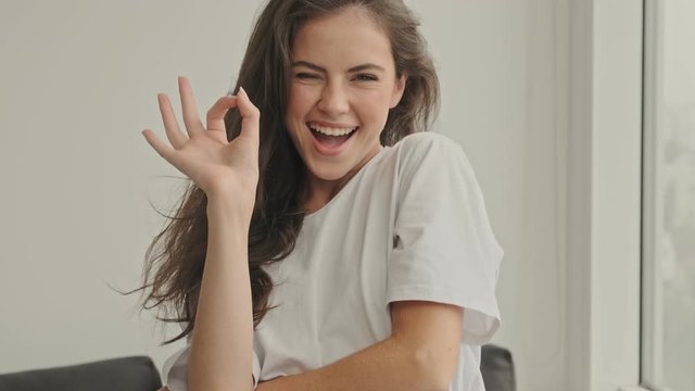 Happy pretty brunette woman showing ok sign and looking at the camera at home
