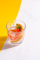 Refreshing cold summer drink in a glass with slice of grapefruit and ice cubes on a duotone yellow...