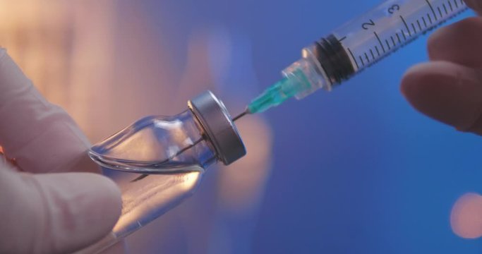 Syringe with needle filling with transparent fluid. Vial filled with vaccine or other medicine. Close-up shot on laboratory background.