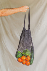 Hand of a man holding a reusable cotton bag with eco vegetables inside. Eco friendly lifestyle. Real fooding concept.