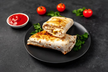 Burrito wraps with chicken and vegetables 
in a black plate , against a background of concrete , 
Mexican shawarma
