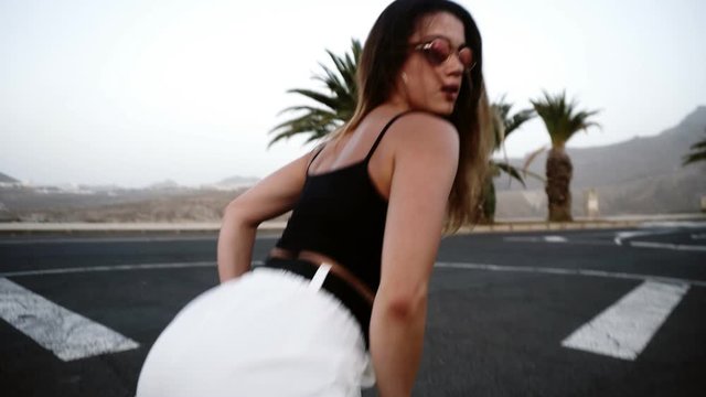 Sexy girl with beautiful body dancing twerk at the resort, tropical area. Girl in sunglasses moves her butt standing on the asphalt. Brunette girl moves her body outdoors. Close up