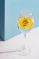 Summer homemade cold cocktail in a glass with lemon slice on a white table with shadow against...