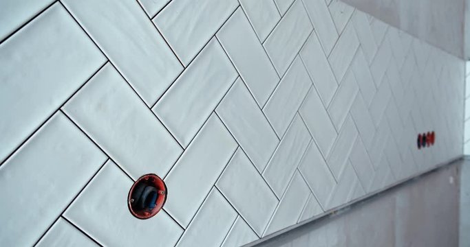 Repair in apartment. White tile laid on the wall with pattern. Ceramic tile master finished his work in future kitchen. Tile is neatly laid, you can proceed to the next stage of work. Finish work