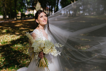 Fototapeta premium Beautiful bride in fashion wedding dress on natural background.The stunning young bride is incredibly happy. Wedding day. A beautiful bride portrait in the forest.