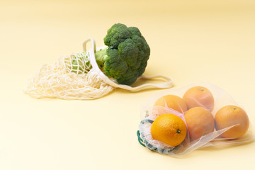 Zero waste food shopping with reusable bags. Flat lay with fruits and vegetables in textile packaging. Broccoli and oranges on yellow background.