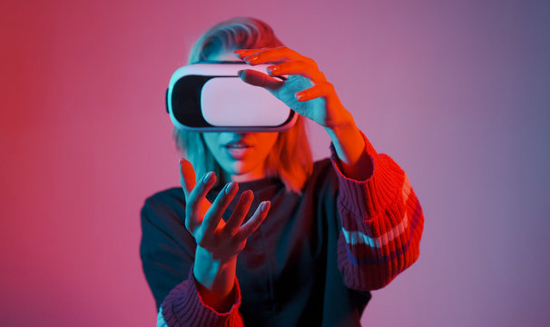 Young woman in VR glasses. A woman immersed in virtual reality makes movements with her hands. Blue and red light falls on a woman on a black background.