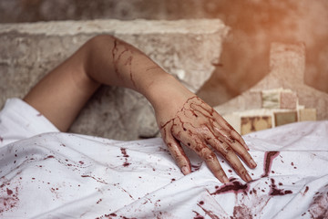Woman wearing a white dress lying on chair with blood stained hands and wearing sets. Halloween...