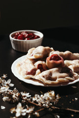 Dumplings with cherries on a black background. European cuisine, recipe. Vertical photo.