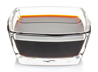Soy sauce in a small transparent glass square bowl isolated on white background