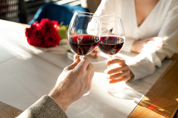 Hands of young man and woman with glasses of red wine over served table