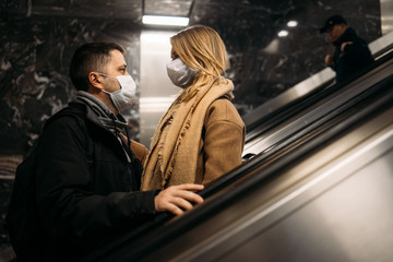 Man and woman looking at each other in medical masks on escalator in subway.