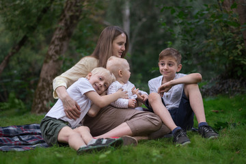 Naklejka na ściany i meble Three happy smiling child sitting in park with mother. Family picnic