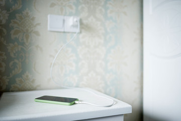 A green smartphone is  charging on the white table.