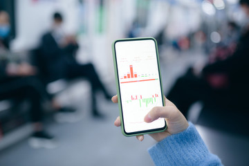 Fototapeta premium Close up of businesswoman checking financial trading data on smart phone in the subway train.