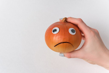 Hand holding sad onion on white background. Napiform onion with funny face and Googly eyes