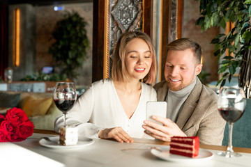 Young couple watching something in smartphone while sitting by served table