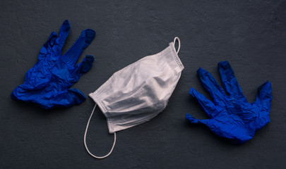 
A white mask and a pair of blue gloves to fight COVID19. Gray background. Horizontal format.