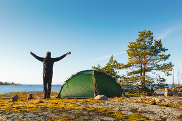Happy man spread his arms on the beach with a green tent. Freedom concept.