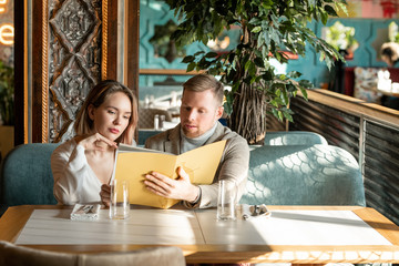 Young romantic couple looking through menu in luxurious restaurant