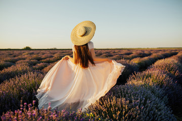 Beautiful young woman walking the field of lavender in Provence, France. Fashion outfit pale rose...