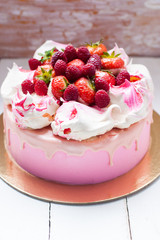 Pink cake with meringue, melted chocolate and fresh raspberries and strawberries.