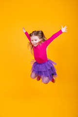 Fototapeta na wymiar Adorable small child girl is jumping and smiling on yellow background
