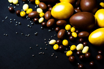 Golden eggs and delicious chocolate easter eggs and yellow sweets on black background