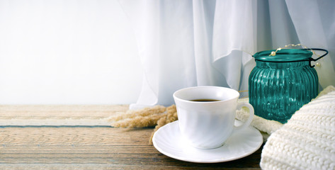 Still life hygge kitchen details on desktop. Coffee cup, blanket and light glass on wooden desk. Mock up autumn relax concept.