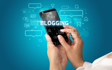 Female hand typing on smartphone with BLOGGING inscription, social media concept