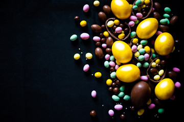 Colorful composition of golden eggs and delicious chocolate easter eggs and colorful sweets on black background. Easter concept