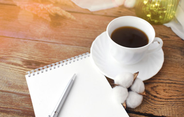 Coffee cup and empty notepad on wooden background. Cozy home workplace or planning concept. Hygge. Fall still life. Sunlight effect.