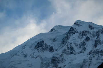 Fototapeta na wymiar A close up view on snow caped Himalayan peak seen from Annapurna Circuit Trek, Nepal. Sharp and steep slopes of the mountain. Clouds behind it. Serenity an peace