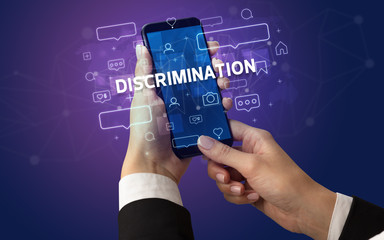Female hand typing on smartphone with DISCRIMINATION inscription, social media concept