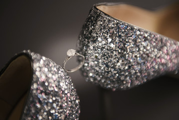 Stylish bride's shoes with high heels, gray shoes, covered with many sequins, shiny heel, next to a gold engagement ring with a stone