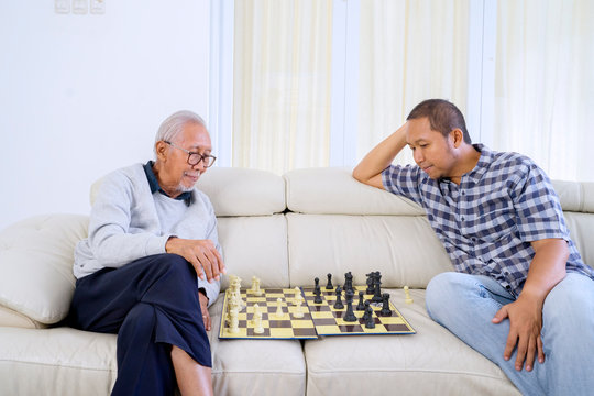Old Man And His Son Playing Chess In Living Room