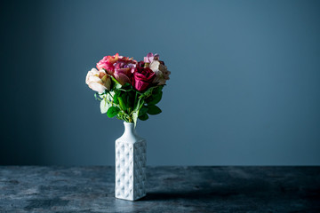Artificial antique roses in vase on dark background.