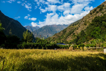 Fototapeta premium Idyllic view on Himalayan valley, Annapurna Circuit Trek. There is a field in the front and a small house in the back. Slopes overgrown with green plants. High mountain chains. Serenity and calmness