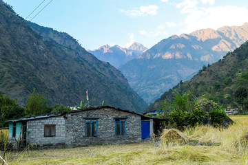 Fototapeta na wymiar A small cottage along Annapurna Circuit Trek in Himalayas, Nepal. There are high mountain chains around it. Steep and barren slopes. Few prayer flags hanged on the rooftops. Serenity and calmness.