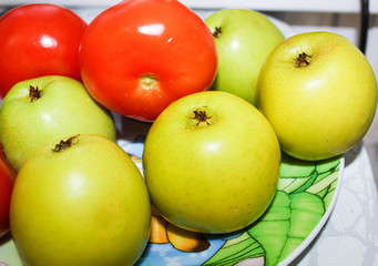 Green apples and red tomatoes on the table at home.