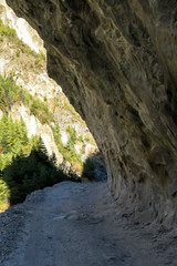 A pathway leading under a hanging mountain wall along Annapurna Circuit Trek, Nepal. Sharp and steep slopes of the mountain. Dangerous hiking. Possibility of a land slid.