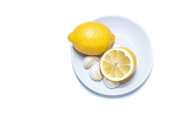 Cloves of garlic. Ripe, juicy, yellow lemon and half a lemon on a white plate. Isolated object on a white background