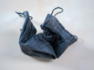 Used crumpled black surgical mask with rubber ear straps. Typical three-layer surgical mask for...