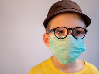cute blonde boy in blue medical mask and glasses is quarantined at home. child coughs heavily and wears mask. concept of fight against the coronavirus epidemic and proper prevention of infections