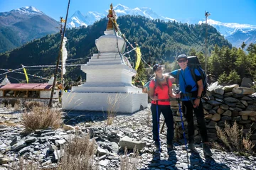 Papier Peint photo Manaslu Couple standing in front of a small white pagoda along Annapurna Circuit Trek in Nepal. They are enjoying the view. Snow caped mountains in the back. Bright and sunny day. Meditation and peace of mind