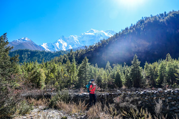 Fototapeta na wymiar A woman trekking along Annapurna Circuit in Nepal. She is enjoying the view and trek. There is a lush green Himalayan valley around her. Snow caped mountains in the back. Happiness and achievement.